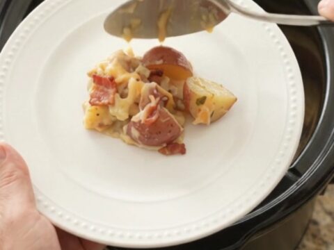 Slow cooker filled with creamy red potato bake topped with melted smoked Gouda and Parmesan