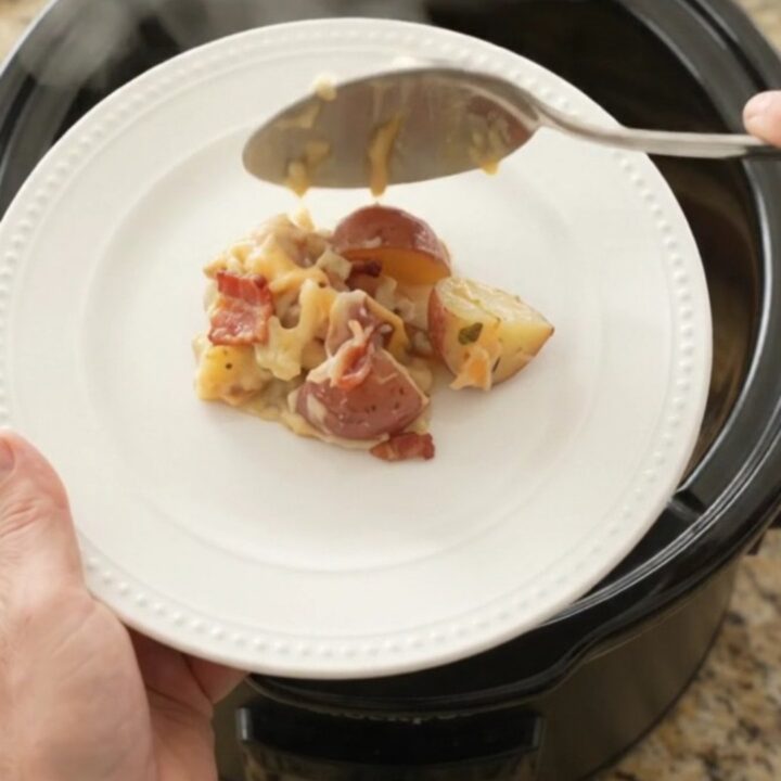 Slow cooker filled with creamy red potato bake topped with melted smoked Gouda and Parmesan