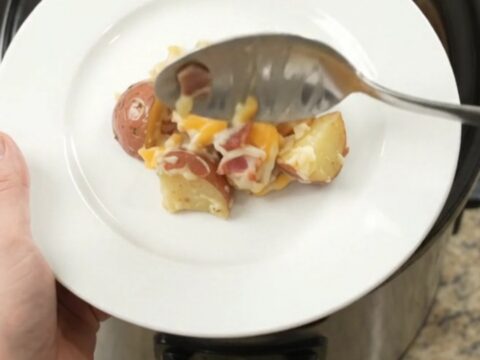 Slow cooker filled with creamy, cheesy red potato bake, topped with melted Colby-Jack cheese and bacon