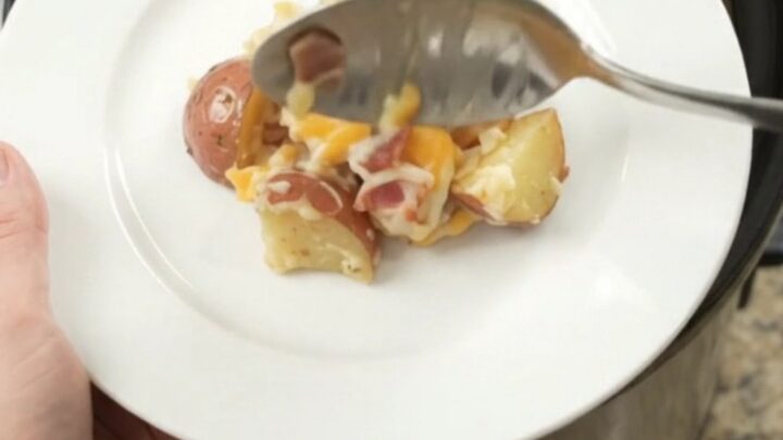 Slow cooker filled with creamy, cheesy red potato bake, topped with melted Colby-Jack cheese and bacon