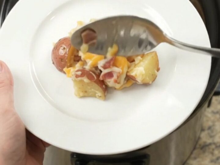Slow cooker filled with creamy, cheesy red potato bake, topped with melted Colby-Jack cheese and bacon