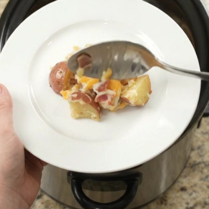 Slow cooker filled with creamy, cheesy red potato bake, topped with melted Colby-Jack cheese and bacon
