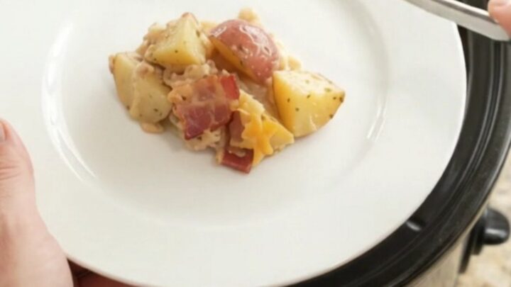 Slow cooker filled with cheesy red potato bake, topped with melted cheddar and bacon.