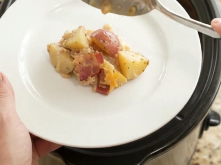 Slow cooker filled with cheesy red potato bake, topped with melted cheddar and bacon.