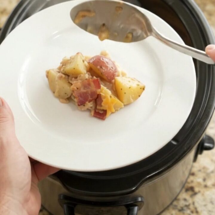 Slow cooker filled with cheesy red potato bake, topped with melted cheddar and bacon.