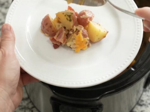 Slow cooker filled with cheesy red potato bake, bubbling and golden on top