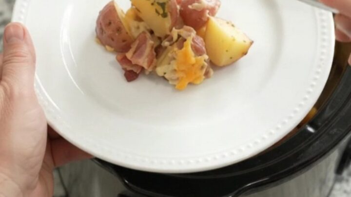 Slow cooker filled with cheesy red potato bake, bubbling and golden on top