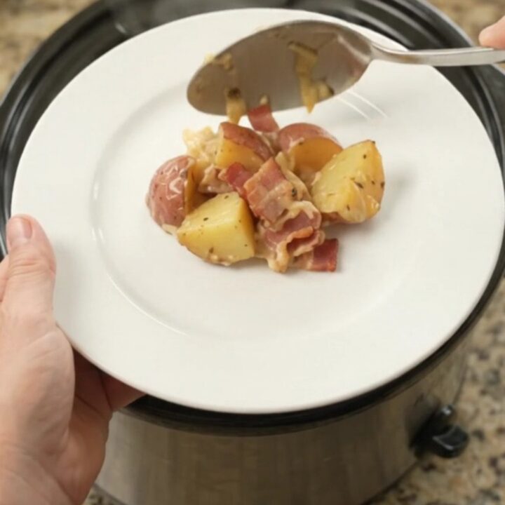 Slow cooker filled with bubbling potato bake topped with melted smoked Gouda and Parmesan