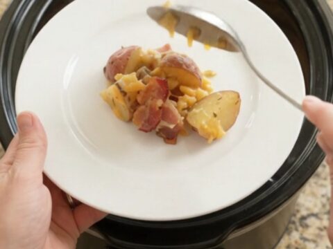 Bubbling cheddar green chile red potato bake in a black slow cooker, golden crust and steam rising