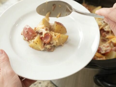 A slow cooker filled with creamy, cheesy red potato bake, topped with melted smoked gouda and Parmesan