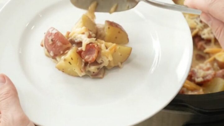 A slow cooker filled with creamy, cheesy red potato bake, topped with melted smoked gouda and Parmesan