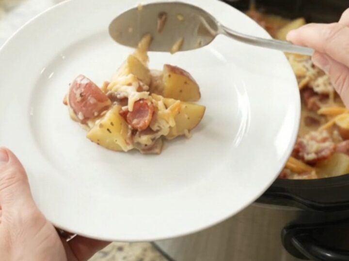 A slow cooker filled with creamy, cheesy red potato bake, topped with melted smoked gouda and Parmesan