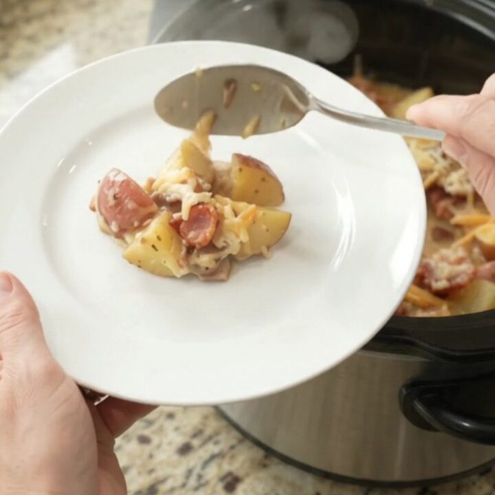A slow cooker filled with creamy, cheesy red potato bake, topped with melted smoked gouda and Parmesan