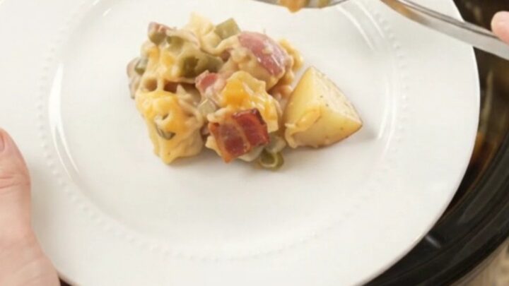 Steaming slow cooker filled with creamy red potato bake topped with melted cheese and bacon bits