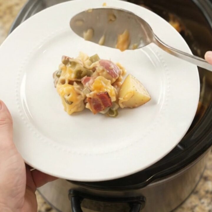 Steaming slow cooker filled with creamy red potato bake topped with melted cheese and bacon bits