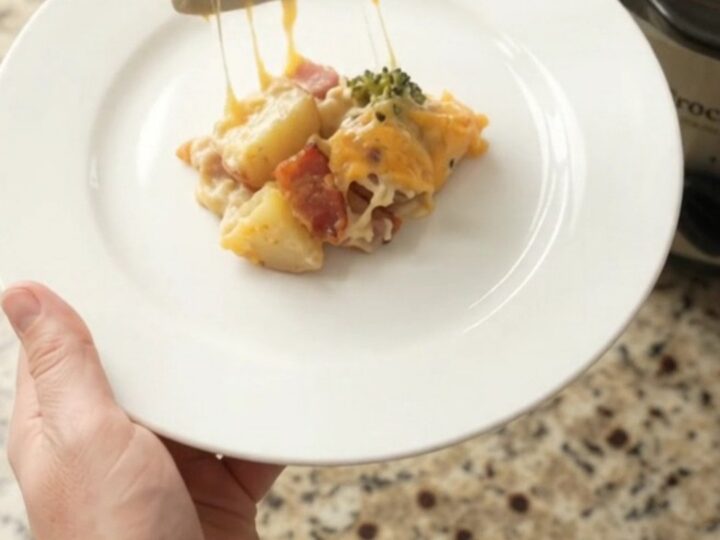 A slow cooker filled with creamy cheddar broccoli potato casserole, topped with melted cheese and steam rising.