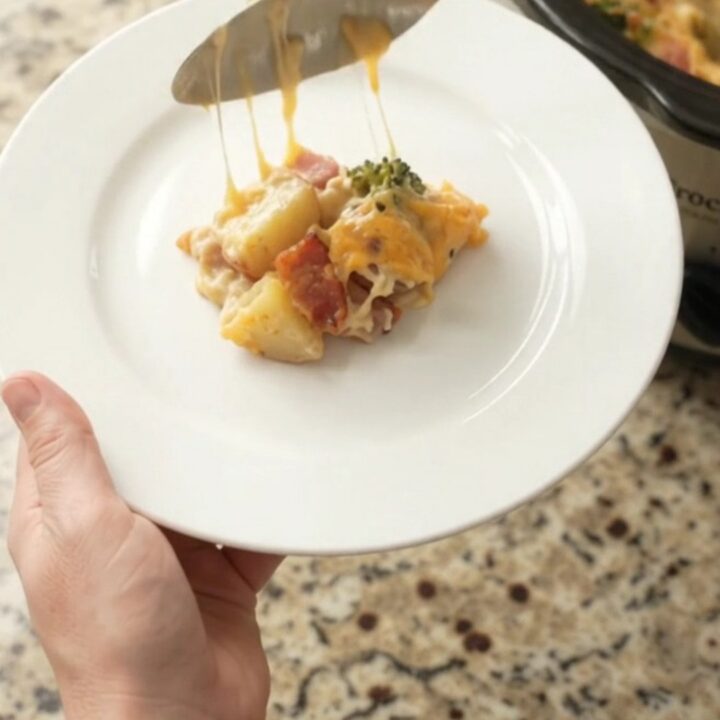 A slow cooker filled with creamy cheddar broccoli potato casserole, topped with melted cheese and steam rising.
