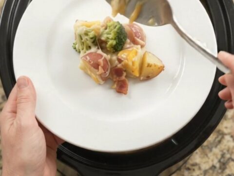 Slow cooker filled with creamy potato bake topped with melted Colby-Jack cheese and broccoli.