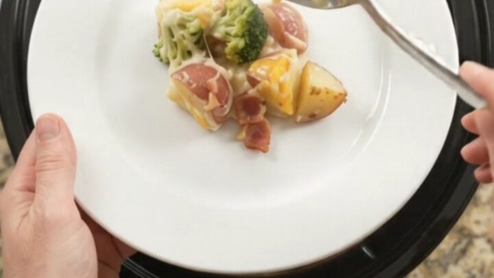 Slow cooker filled with creamy potato bake topped with melted Colby-Jack cheese and broccoli.