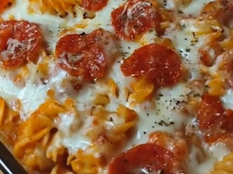 A portion of pizza pasta casserole being lifted with a spatula, showing long strings of melted mozzarella cheese.