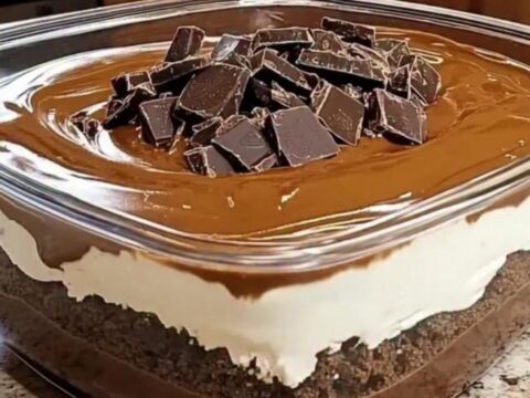 A square glass dish filled with layers of chocolate cookie crumbs, fluffy cream, and glossy ganache.