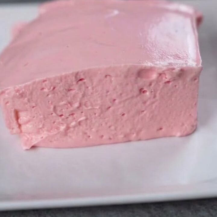 A thick, airy slice of pink strawberry fluff cake on a white square plate.