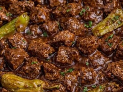 A close-up of tender beef cubes in a rich, dark gravy with whole pepperoncini peppers inside a slow cooker.