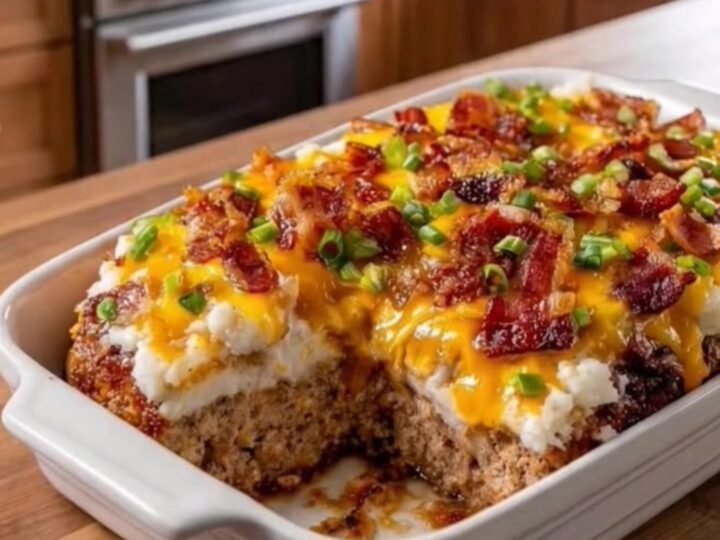 A slice of cheesy loaded meatloaf casserole on a white plate, showing layers of meat, potatoes, and melted cheese.