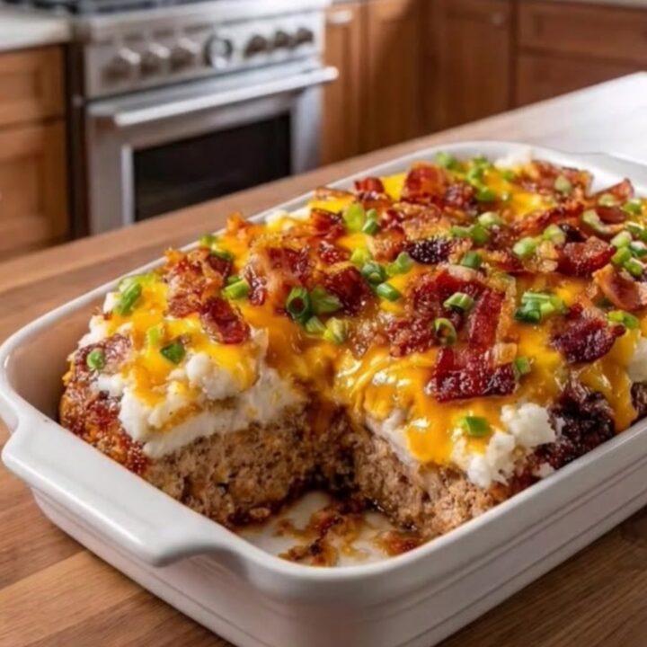 A slice of cheesy loaded meatloaf casserole on a white plate, showing layers of meat, potatoes, and melted cheese.