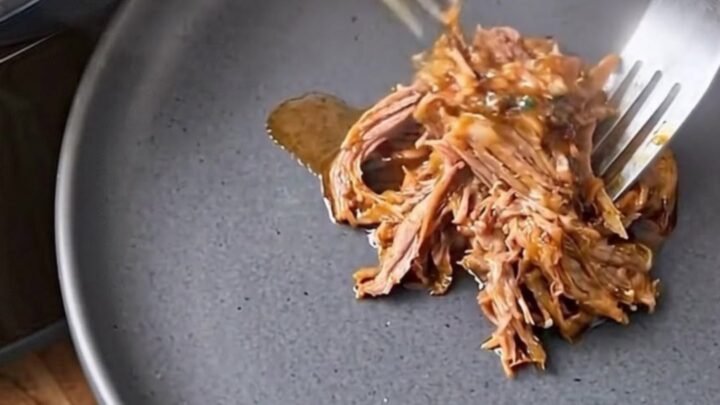 Two forks shredding tender steamed corned beef on a dark plate.