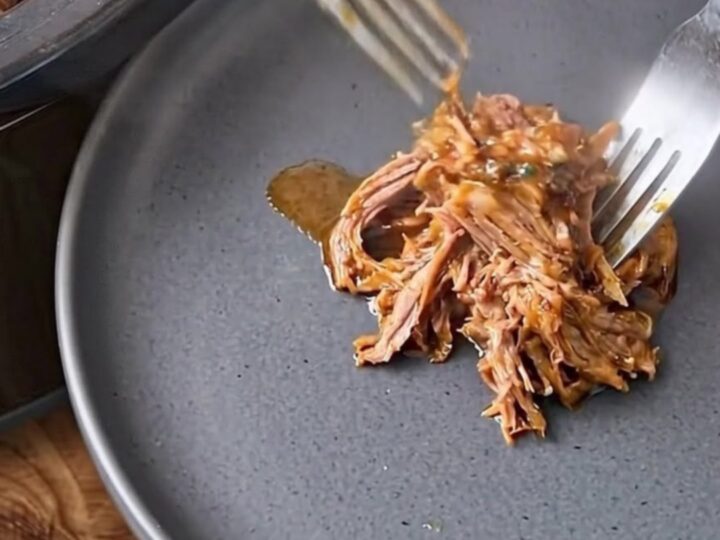 Two forks shredding tender steamed corned beef on a dark plate.