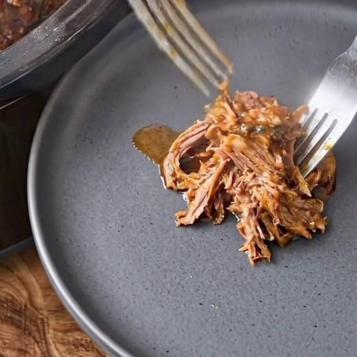 Two forks shredding tender steamed corned beef on a dark plate.