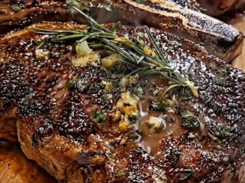 A perfectly seared bone-in ribeye resting on a wooden board, topped with melting garlic herb butter and fresh rosemary.