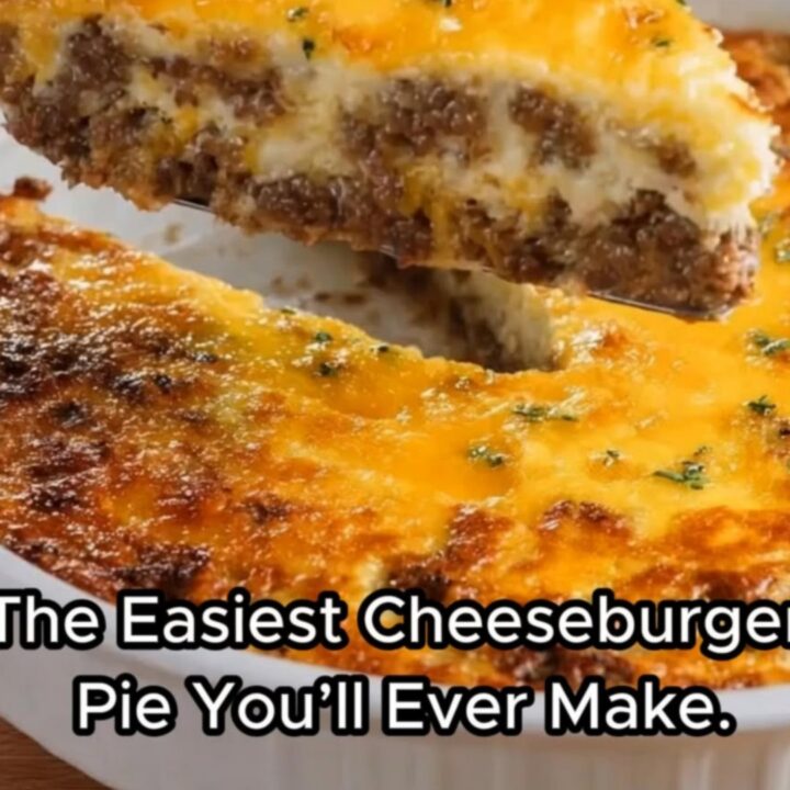 A thick, steaming slice of golden-brown cheeseburger pie being lifted from a white ceramic baking dish.