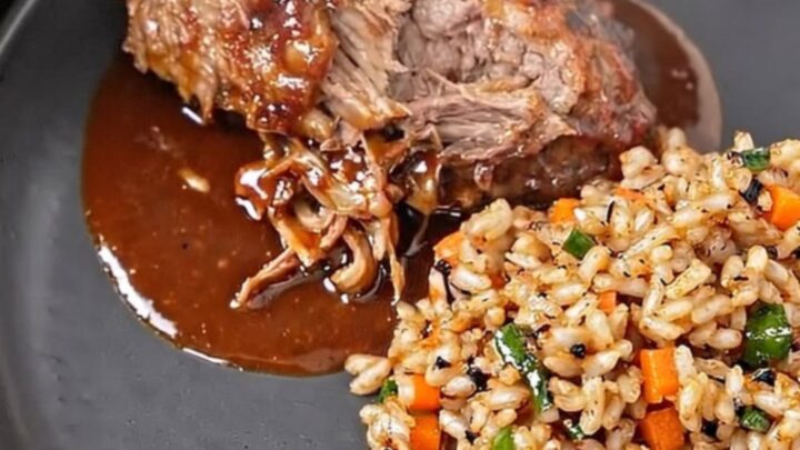 A close-up of tender BBQ ribs on a dark plate, showing glossy sauce and steam rising.