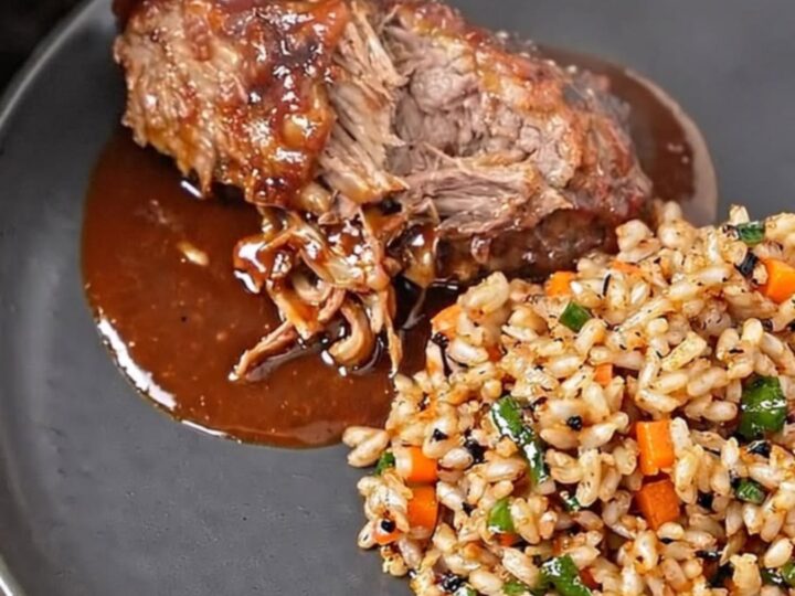 A close-up of tender BBQ ribs on a dark plate, showing glossy sauce and steam rising.