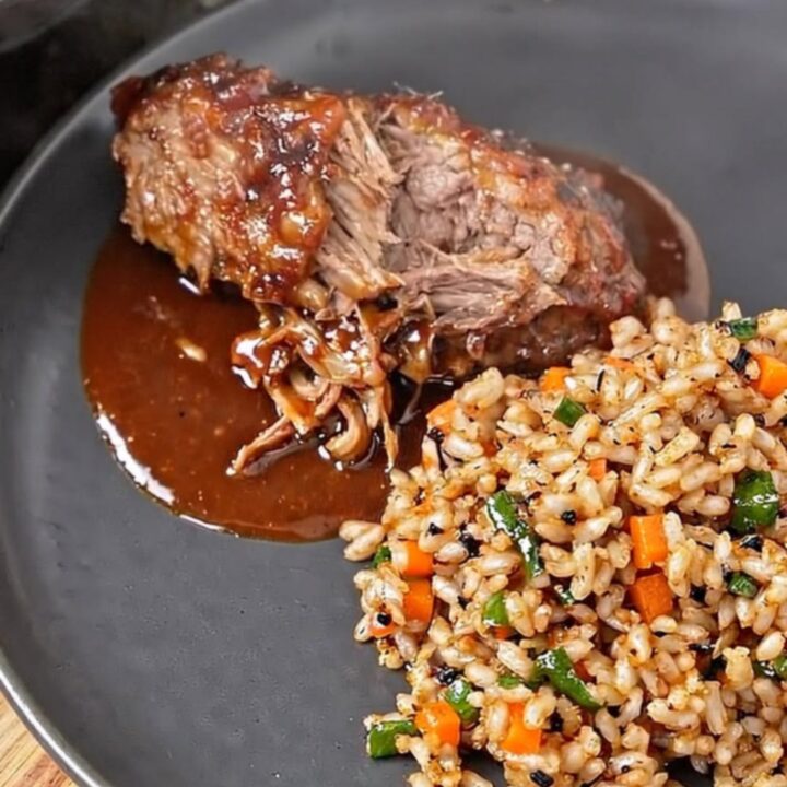 A close-up of tender BBQ ribs on a dark plate, showing glossy sauce and steam rising.