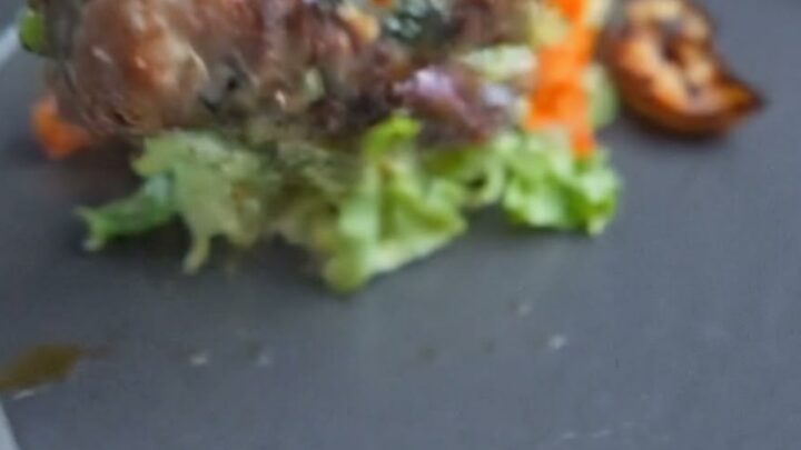 A close-up of glazed beef rolls served on a dark plate with fresh greens, showing a glistening surface.