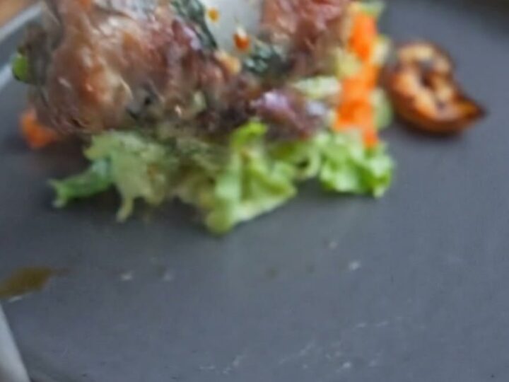 A close-up of glazed beef rolls served on a dark plate with fresh greens, showing a glistening surface.