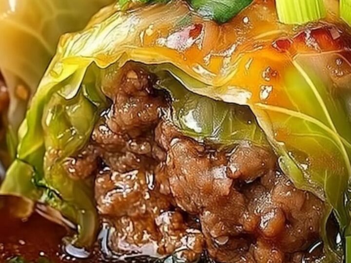 A rustic plate featuring glossy, amber-glazed stuffed cabbage rolls garnished with fresh scallions and sesame seeds.