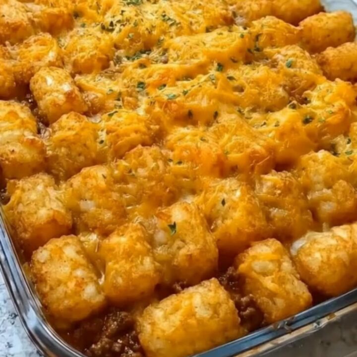A steaming scoop of cheeseburger tater tot casserole being lifted with a spatula, showing melted cheese