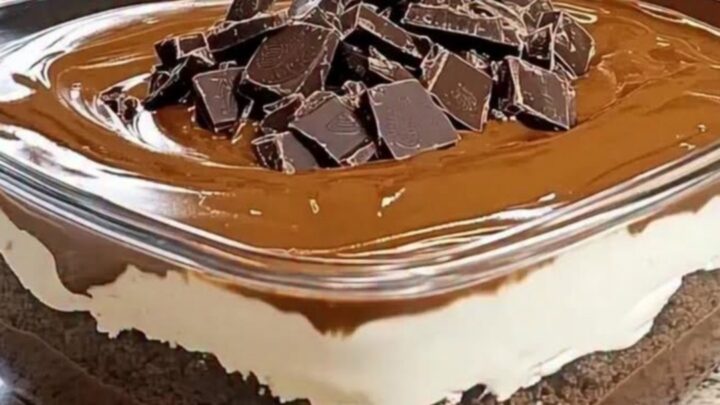 Cold chocolate layered dessert in a square glass dish displaying crumb, cream, and ganache layers.