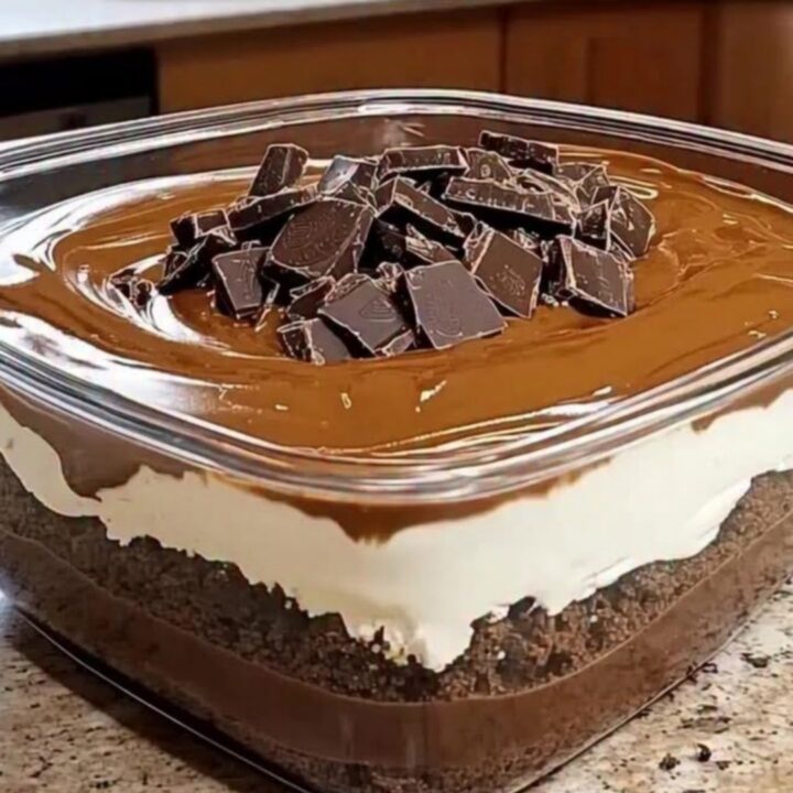 Cold chocolate layered dessert in a square glass dish displaying crumb, cream, and ganache layers.