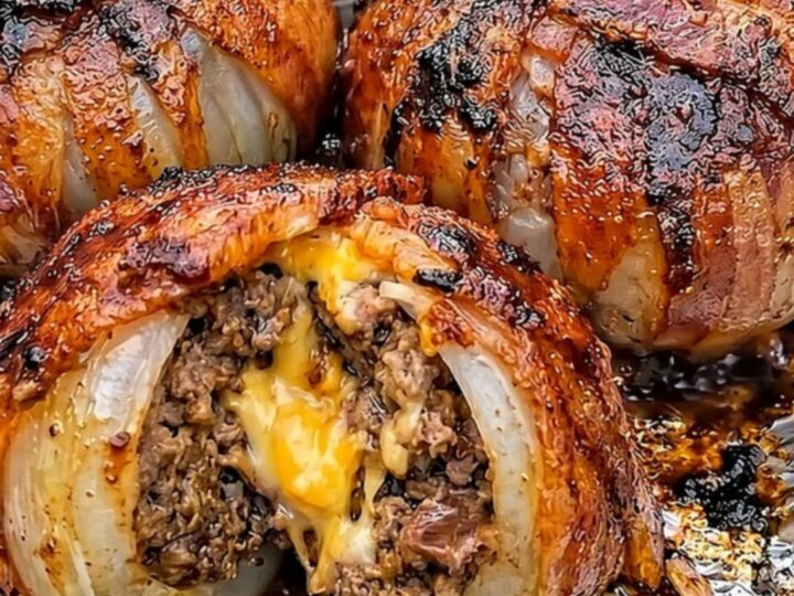 A close-up of a bacon-wrapped stuffed onion sliced in half, revealing the juicy beef and molten cheddar center.