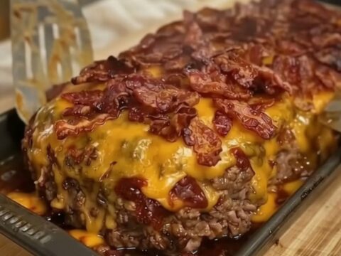 A close-up of a juicy meatloaf slice being lifted with a spatula, showing melted cheddar cheese and crispy bacon.