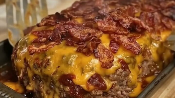 A close-up of a juicy meatloaf slice being lifted with a spatula, showing melted cheddar cheese and crispy bacon.