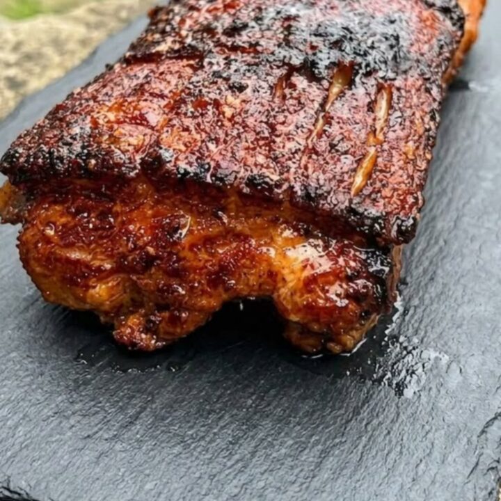 A close-up shot of a perfectly smoked pork belly with a dark, caramelized bark on a slate board.