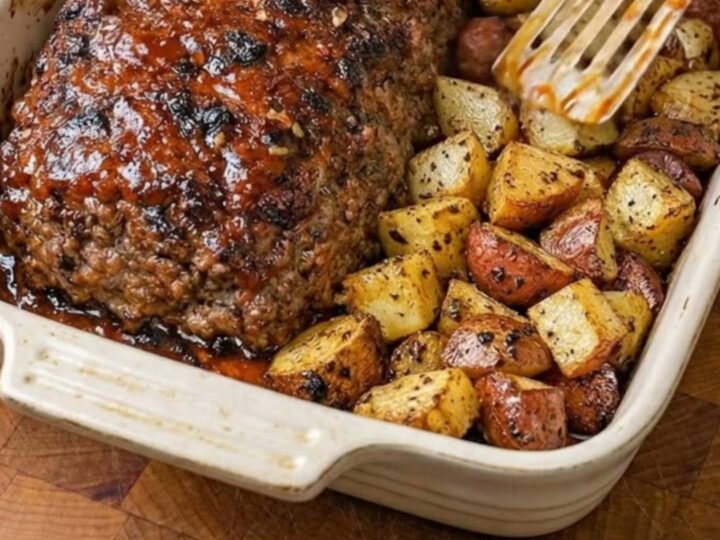 A glistening, glazed meatloaf with roasted potatoes on a wooden board.