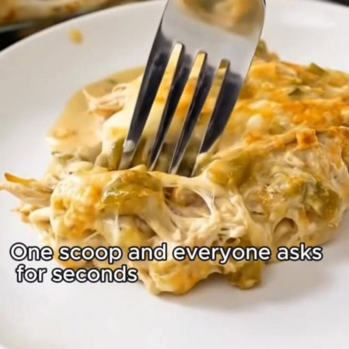 A fork lifting a cheesy, creamy bite of green chile chicken enchilada casserole from a white plate.