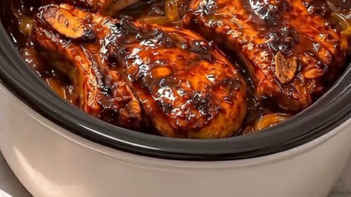 Four caramelized honey garlic pork chops resting in a slow cooker with steam rising.